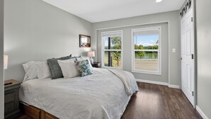 A bedroom with a large bed, two windows, a nightstand, and a door.