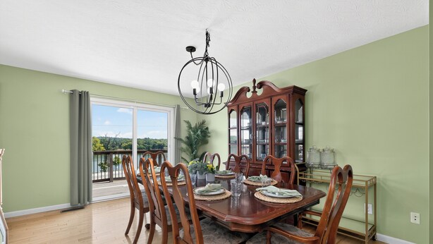 A dining room with a wooden table set for four, surrounded by chairs, a chandelier, and a wooden cabinet with glass doors.