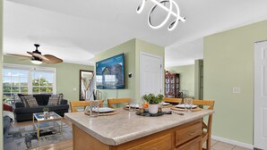 A spacious living area with a large window, a ceiling fan, and a dining area with a kitchen island.