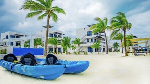 A beach with two blue kayaks, palm trees, and modern buildings with balconies and large windows. - All Shades of Blu -Best Resort in Caye Caulker (Caye Caulker)