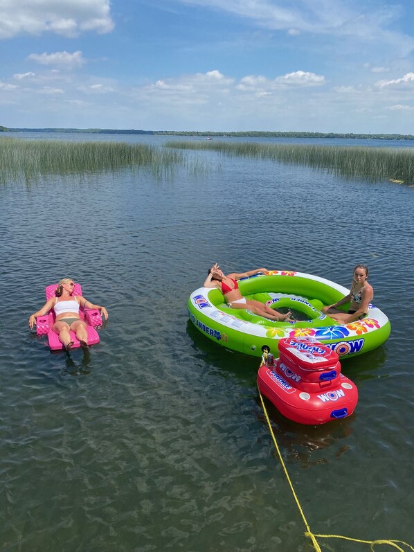 Two inflatable water floats in a body of water with a distant shoreline and marshy area.