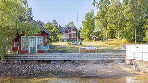 Una propiedad junto al lago con un muelle de madera, una cabaña roja y una casa más grande con balcón.