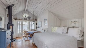 Un dormitorio acogedor con una cama grande, un aparador, una mesa con sillas, una chimenea y vistas al exterior.