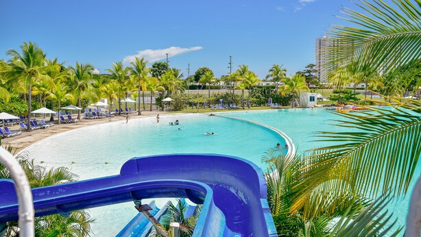 Un espace piscine doté d’un toboggan, de palmiers et de chaises longues.