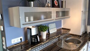 Ett modernt kök med en diskho i rostfritt stål, en kaffebryggare och en krukväxt.