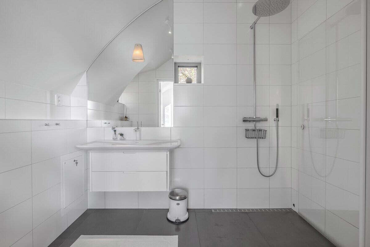 A modern bathroom with a white tiled shower, a sink, and a toilet.