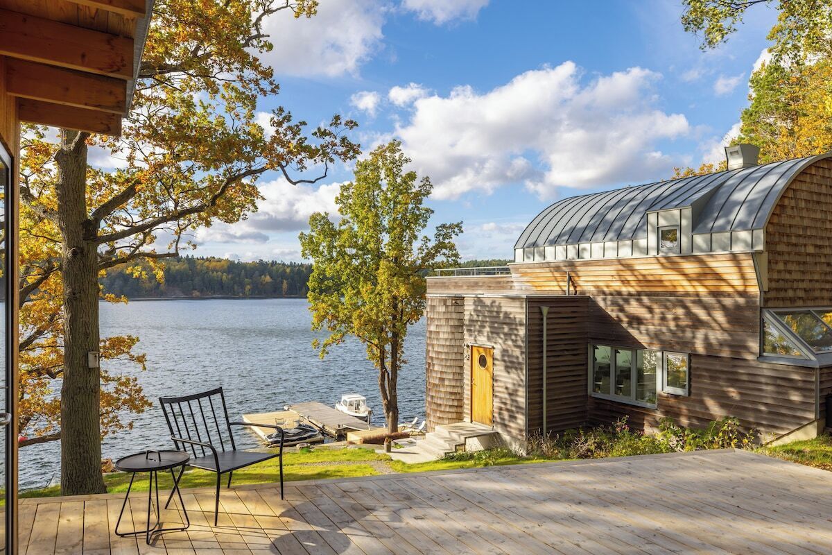A modern house with a curved roof, a deck, and a view of a lake.