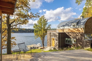 Una casa moderna con techo curvo, una terraza y vista a un lago.