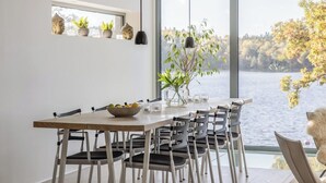 A dining area with a large window overlooking a lake, a wooden table, and several chairs.