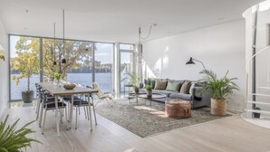 A modern living room with a dining area, large windows, and a view of a lake.