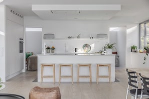 Une cuisine moderne dotée d’un îlot central, de tabourets en bois et d’un coin repas avec des chaises.