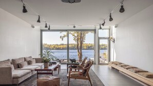 A modern living room with a large window overlooking a lake, furnished with a sofa, chairs, and a coffee table.