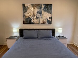 Une chambre à coucher avec un grand lit, deux tables de chevet avec des lampes et un tableau abstrait accroché au mur.
