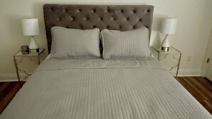 A neatly made bed with a tufted headboard, two bedside lamps, and a wall-mounted abstract art piece.