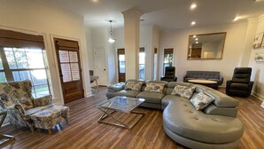 A spacious living room with a large sectional sofa, a glass coffee table, and a patterned armchair.
