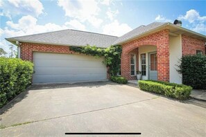 Une maison de plain-pied avec un garage, une façade en briques et un petit porche à l’avant.