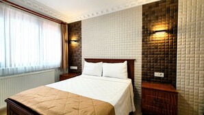 Quarto de hotel com uma cama, mesa de cabeceira, luminária na parede e janela com cortinas.