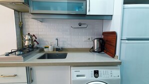 Uma cozinha compacta com pia de aço inoxidável, micro-ondas embutido, lava-louças Samsung e tábua de corte de madeira.