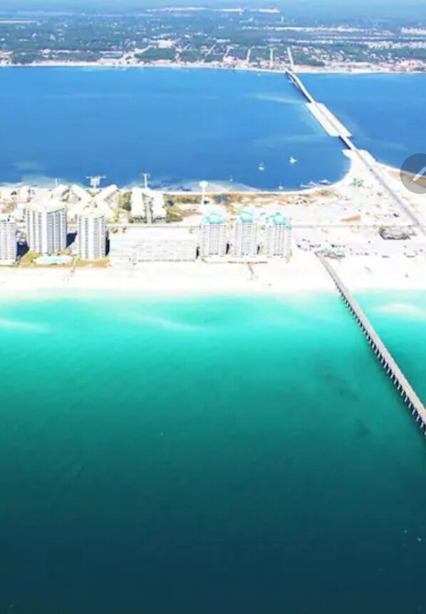 An aerial view of a coastal area with a long pier extending into the water, surrounded by high-rise buildings and a sandy beach. - Bahia Breeze Townhouse ~ Sleeps 8~ Pets Welcome (Navarre)