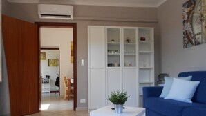 Una sala de estar con un sofá azul, una mesita auxiliar blanca con una planta, y un aparador blanco con estantes.