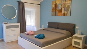 Un dormitorio con cama, cómoda, mesita de noche, espejo y ventana con cortinas.