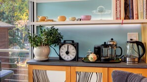 Una cocina con vista al exterior, estantes con vajilla, un reloj y una cafetera.