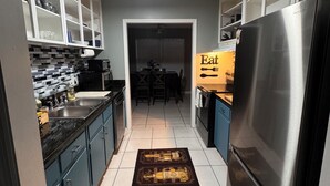 A kitchen with dark cabinets, a stainless steel refrigerator, and a tiled floor. - Work Crew Friendly Housing (Tallahassee)