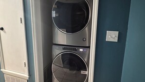 A laundry room with two stacked washing machines, a door, and a light switch on the wall. - Work Crew Friendly Housing (Tallahassee)