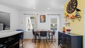 A dining area with a wooden table and chairs, a black cabinet with decorative items, and a large wall clock.