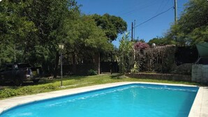 A rectangular swimming pool with a tiled edge, surrounded by a grassy area and trees.