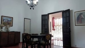 A dining area with a table and chairs, a chandelier, a cabinet with a lamp, and a door with a patterned curtain.