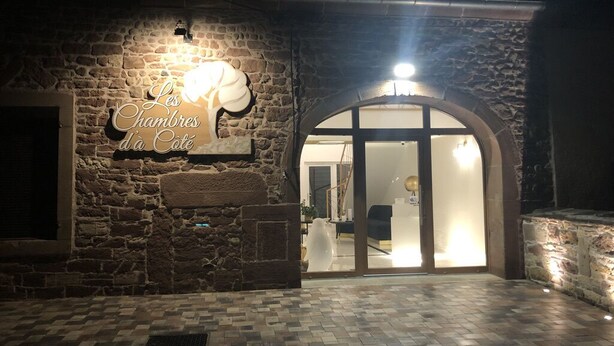 Un edificio de piedra con un letrero que dice "Les Chambres d'à Côté" y una entrada con puertas de vidrio.
