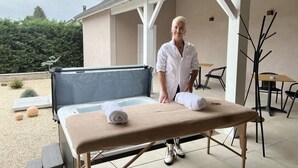 Un espacio de spa con una mesa de masaje, una bañera de hidromasaje y un área de descanso con sillas y una mesa.