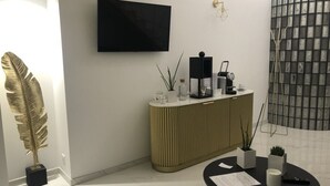 Una sala de estar moderna con un televisor de pantalla plana, un panel decorativo en la pared, una mesa de centro negra con un control remoto y una planta en maceta.