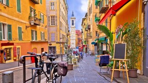 A narrow street with buildings on either side, a bicycle parked on the left, and a small easel with a blank canvas on the right. - Cosy new apartment (Nice)
