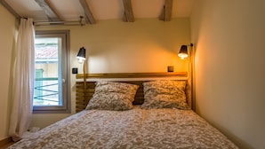 A bedroom with a bed, two bedside lamps, a window with curtains, and a wooden ceiling. - Cosy new apartment (Nice)