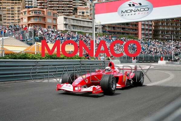 A red Formula 1 car on a race track with a crowd in the background and a large 'MONACO Grand Prix' sign.