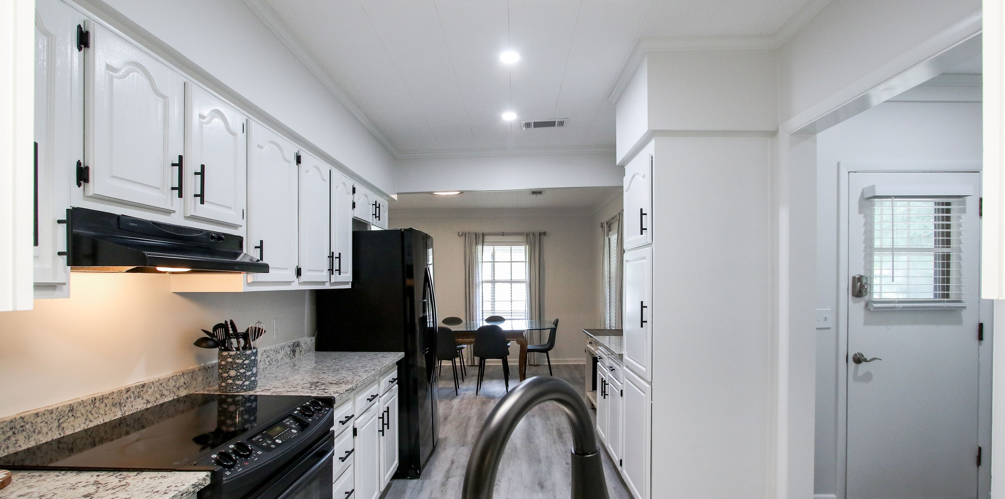 A kitchen with white cabinets, a black refrigerator, and a dining area with a table and chairs.