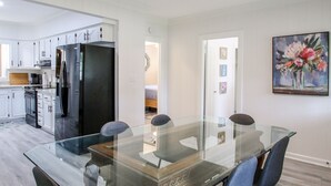 Eine moderne Küche mit weißen Schränken, einem Edelstahl-Kühlschrank und einem Glastisch mit Stühlen.