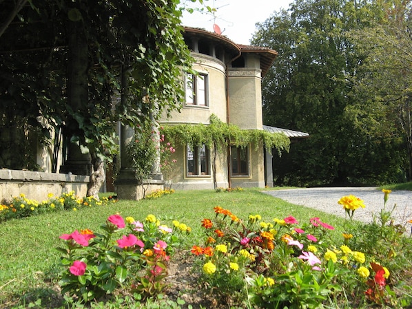 Un bâtiment doté d’une façade en pierre, d’un toit incurvé et d’un jardin aux fleurs multicolores.