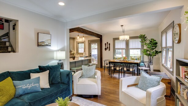 A spacious living room with a teal sofa, white armchairs, and a coffee table. A dining area with a wooden table and chairs is visible in the background. - Renovated Lubbock Home - Walk to Texas Tech! (Lubbock)