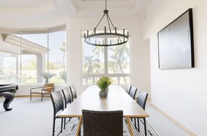 Une salle de conférence avec une longue table, des chaises, un lustre, de grandes fenêtres et un tableau encadré au mur.