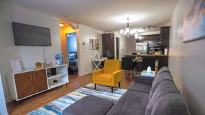 Una sala de estar con un sofá gris, un sillón amarillo y un televisor montado en la pared.