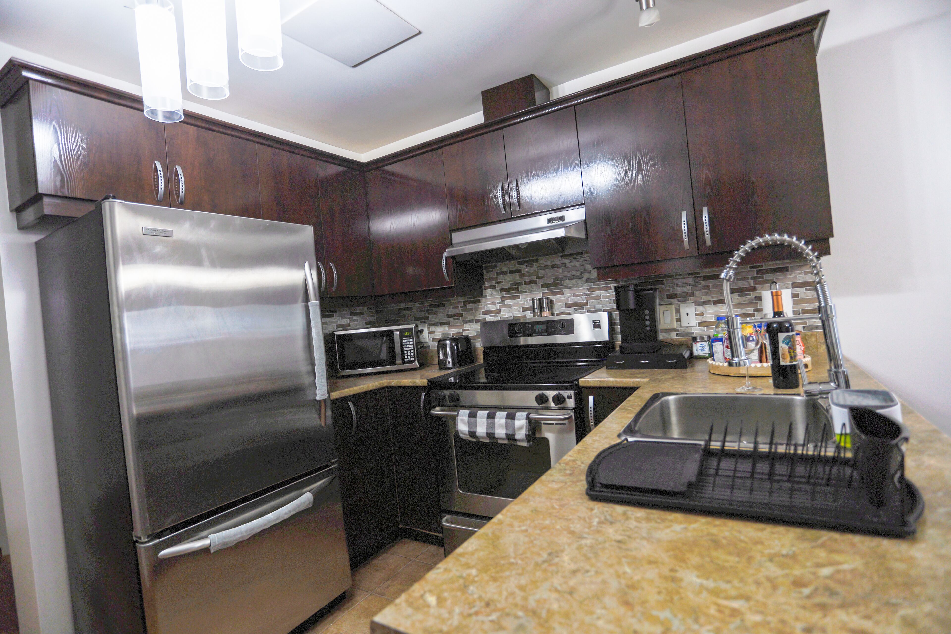 A modern kitchen with stainless steel appliances, dark wood cabinets, and a granite countertop.