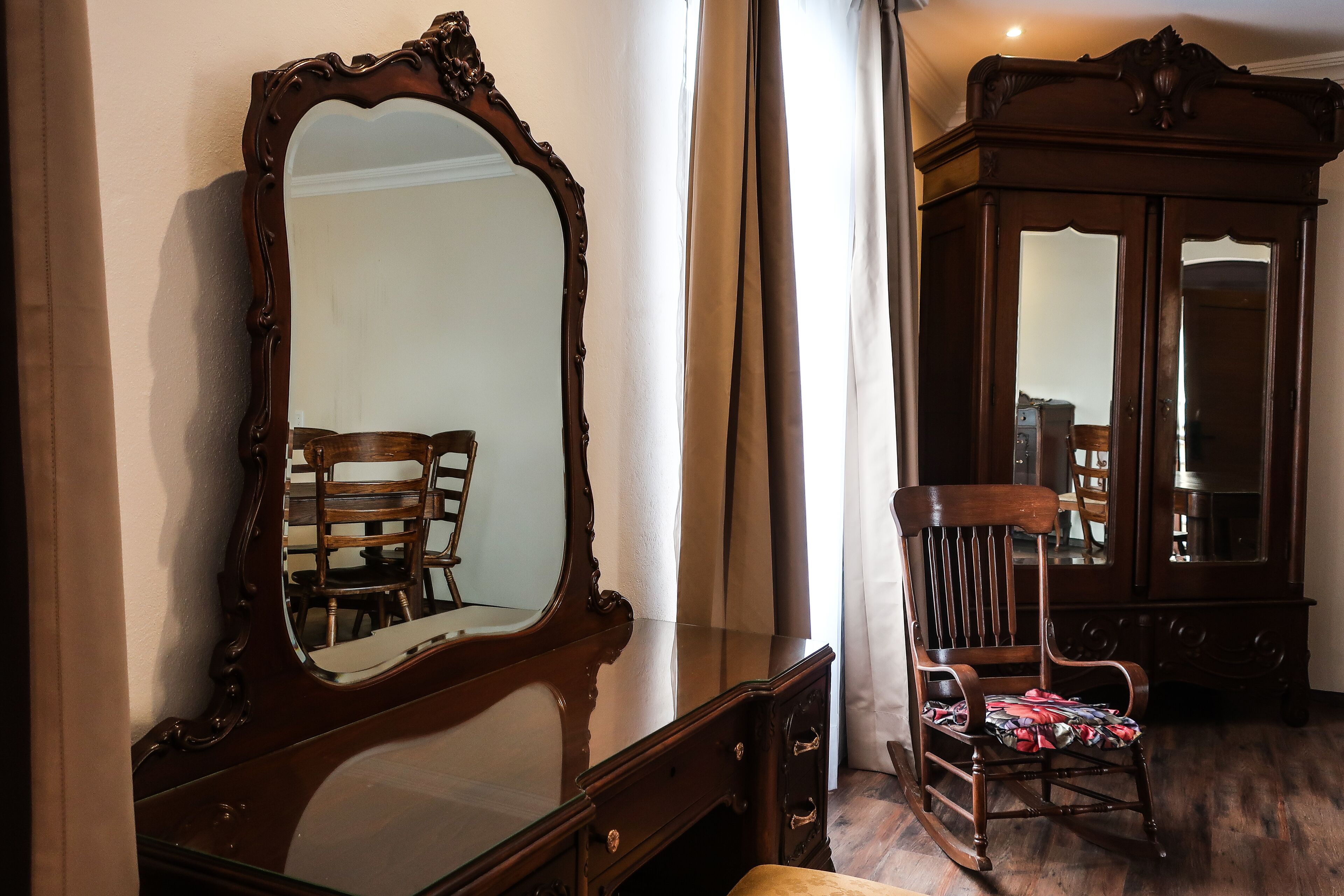 Une pièce comprenant un grand miroir décoratif, un fauteuil à bascule en bois et un buffet en bois foncé.