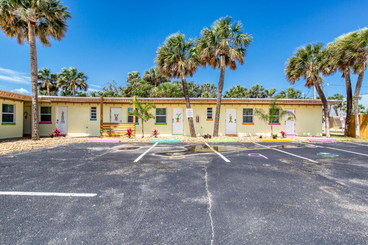 Ein Motel mit mehreren Zimmern, einem Parkplatz und Palmen.