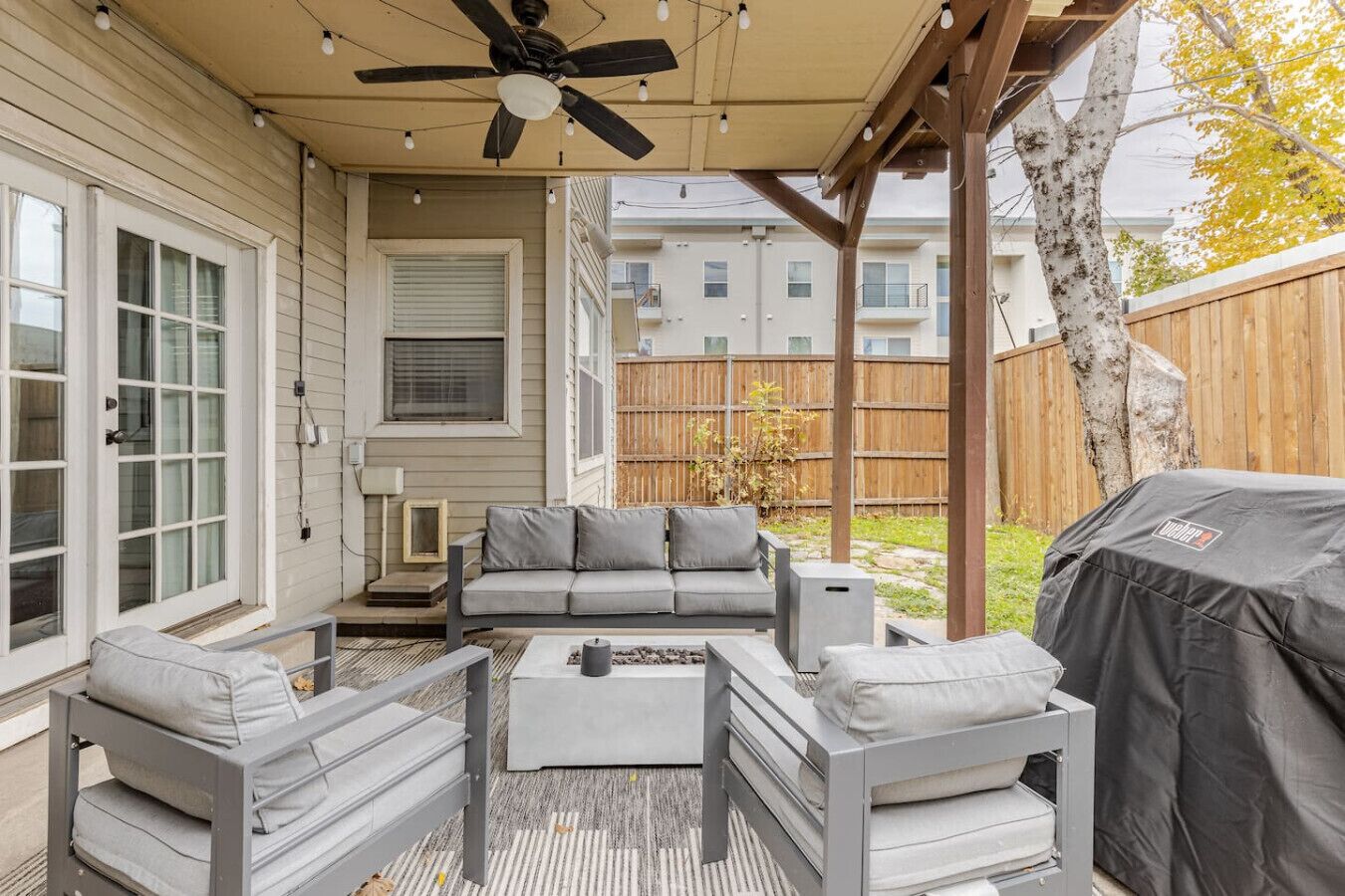 A covered patio with a ceiling fan, a gray sofa set, a coffee table, and a grill.