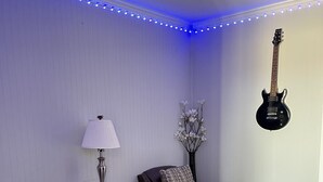 Una sala de estar con un sofá de cuero marrón, un mueble de madera para entretenimiento, una lámpara, un jarrón con flores y una guitarra en la pared.