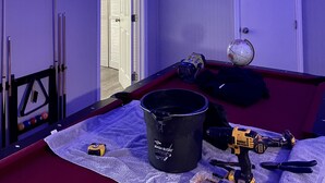 Una habitación con ventilador de techo, luces LED, un cuadro enmarcado, un globo terráqueo, un cubo y una herramienta eléctrica sobre un sofá rojo.