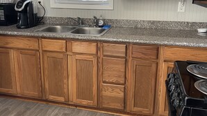 Una cocina con gabinetes de madera, encimera de granito, cafetera, fregadero y estufa.